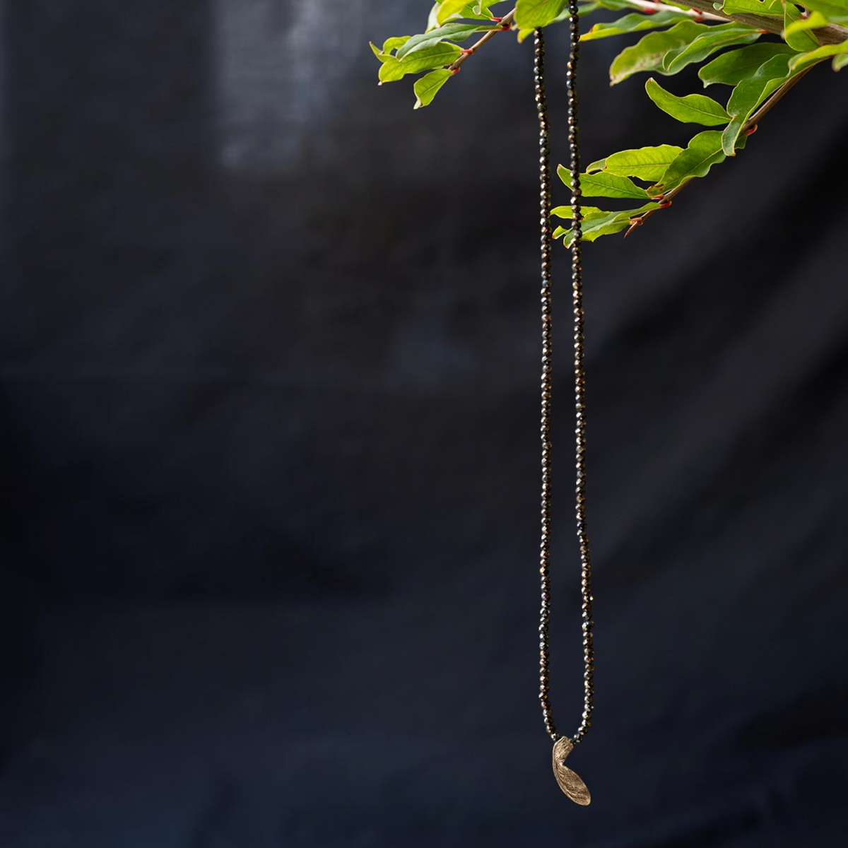Collana MandalaT con ciondolo a forma di seme di acero dorato su una lunga catena di perline scure sfaccettate