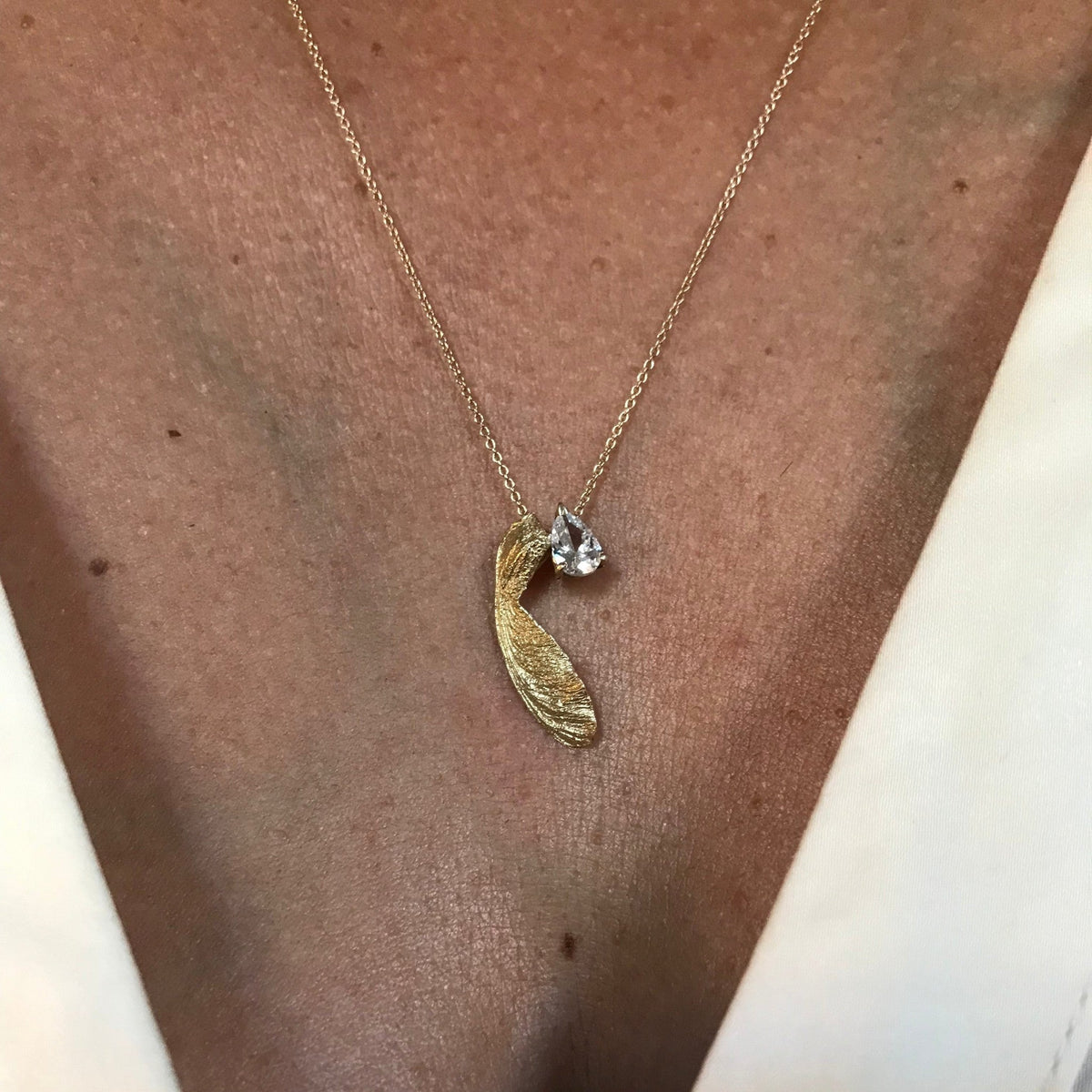 Collana MandalaT in oro con ciondolo a forma di seme di acero e piccolo zircone luminoso indossata al collo