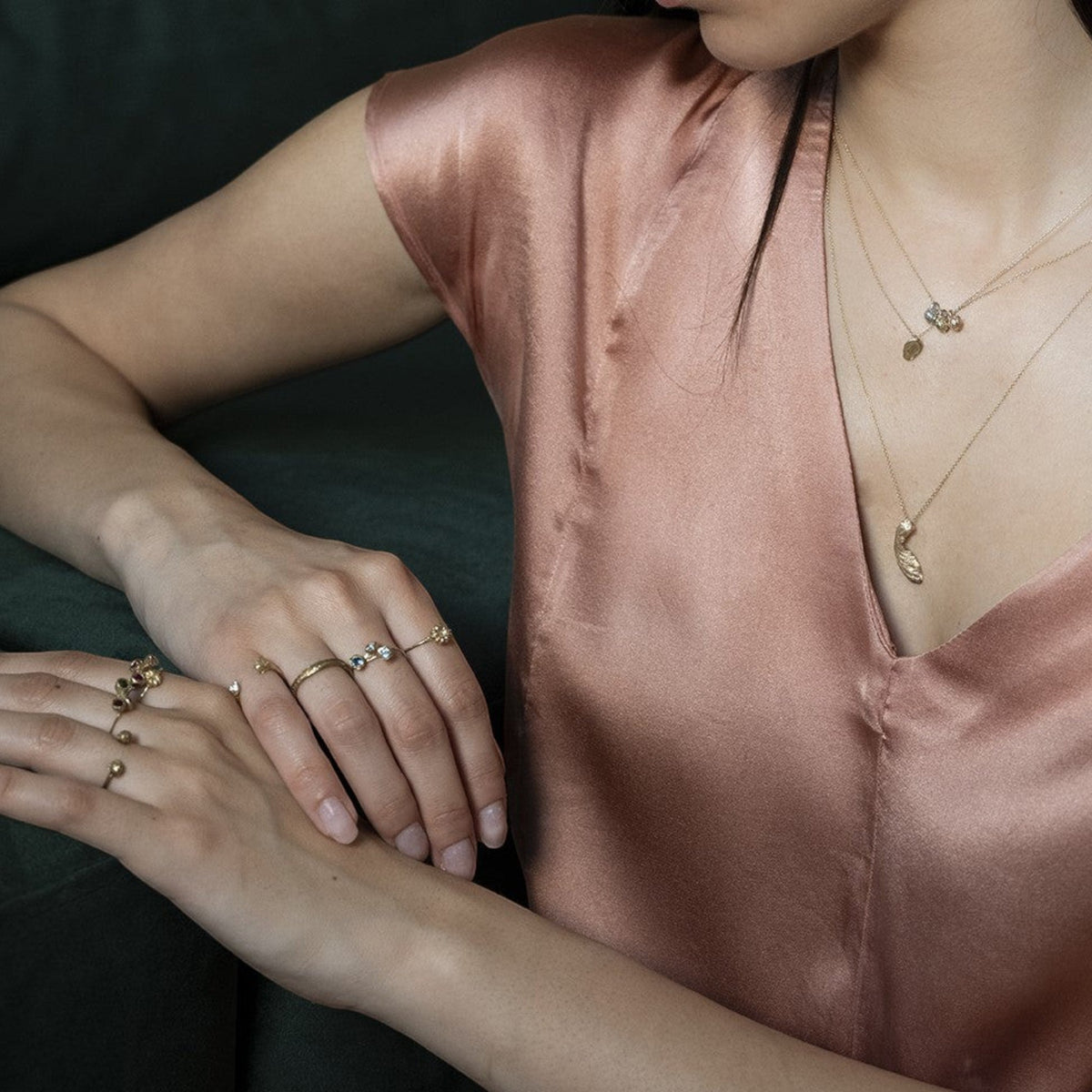 Collana Seme di Acero MandalaT in oro con ciondolo a forma di seme, indossata con anelli sottili su abito di seta
