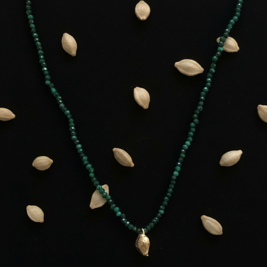Collana MandalaT con perline sfaccettate di Malachite e ciondolo dorato a forma di seme di limone su sfondo nero