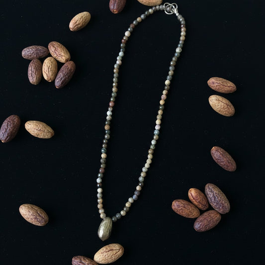 Collana MandalaT con perline sfaccettate nei toni della terra e ciondolo a forma di seme di ulivo su sfondo nero