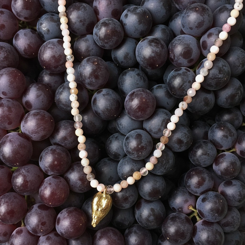 Collana MandalaT con perline di Opale rosa e ciondolo a forma di seme d'uva in oro su sfondo di uva nera fresca