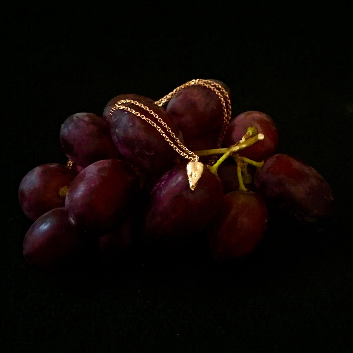 Collana MandalaT con ciondolo a forma di seme d'uva in oro rosa su un grappolo di uva rossa fresca