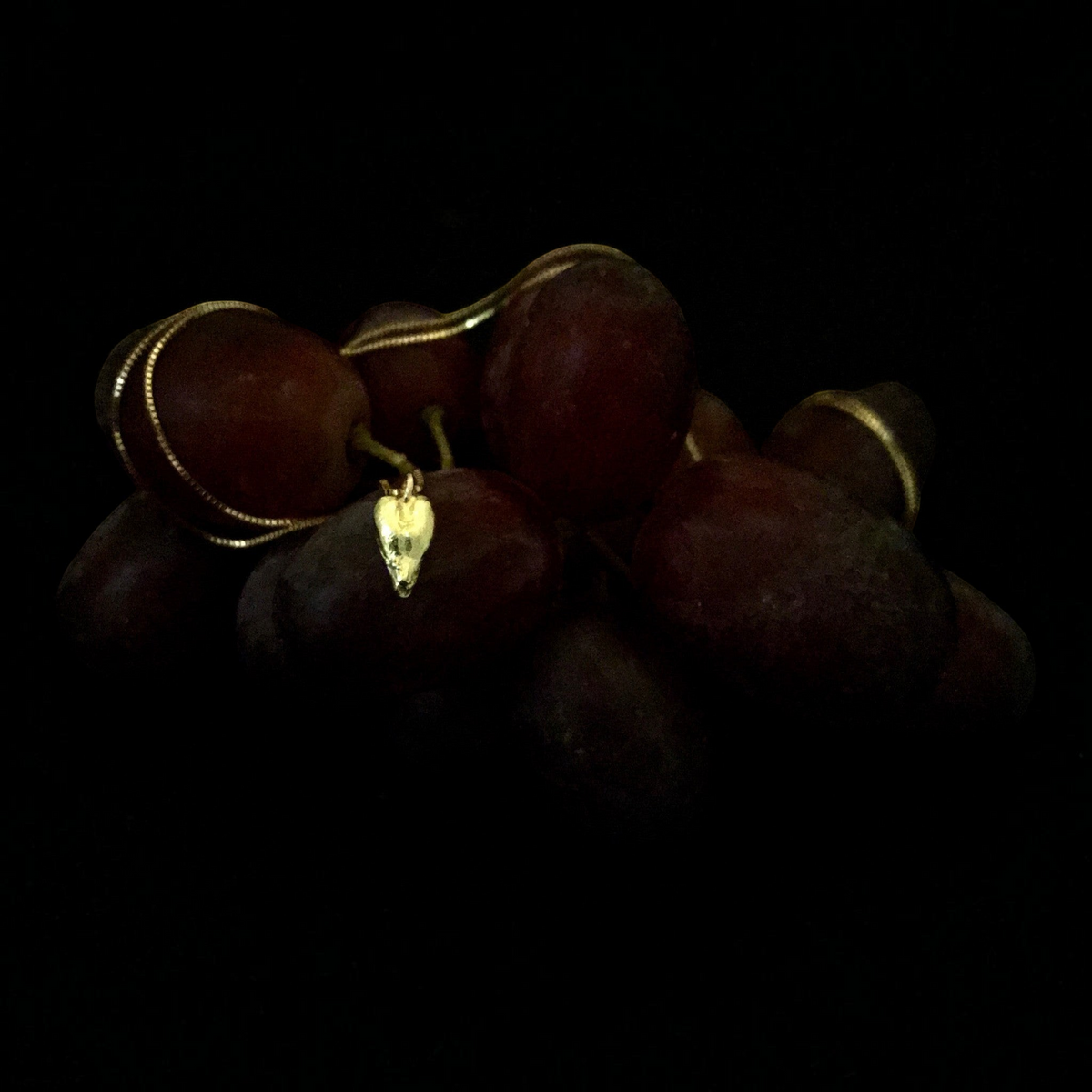 Collana MandalaT con ciondolo a forma di seme d'uva in oro su un grappolo d'uva rossa su sfondo nero