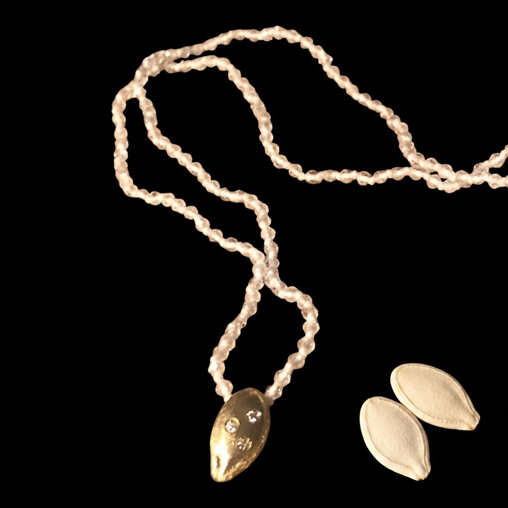 Collana MandalaT con ciondolo a forma di seme di zucca dorato e diamanti con catenina di cristallo di rocca trasparenti annodati con filo bianco su sfondo nero