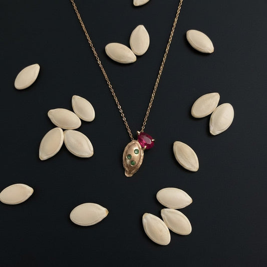 Collana MandalaT a forma di seme di zucca in oro con pietra rossa e piccoli smeraldi su sfondo nero