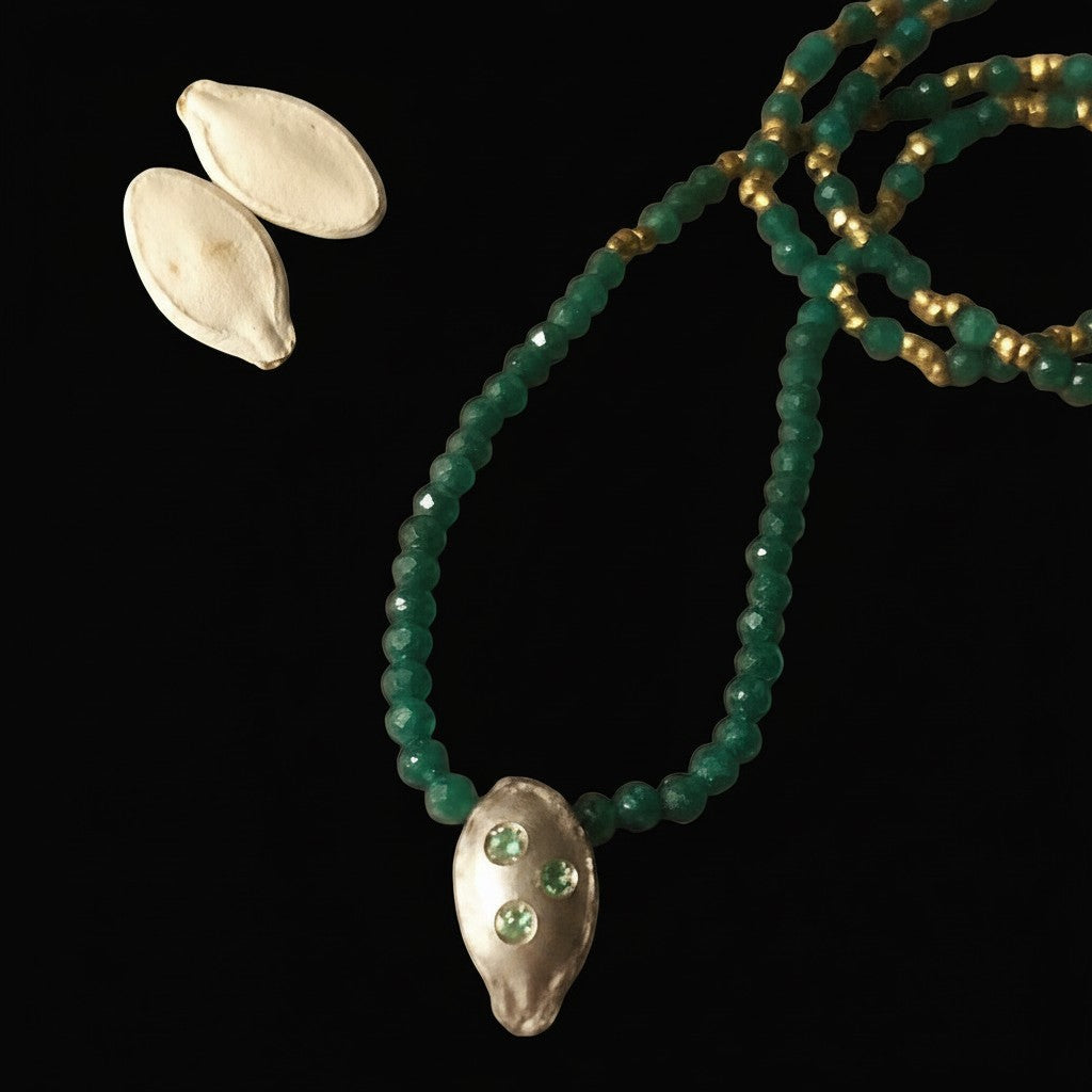 Collana MandalaT con ciondolo a forma di seme di zucca in metallo, pietre verdi e dettagli dorati su sfondo nero