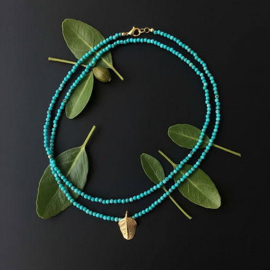 Collana MandalaT con turchesi e ciondolo a forma di foglia di cappero in bronzo su sfondo nero