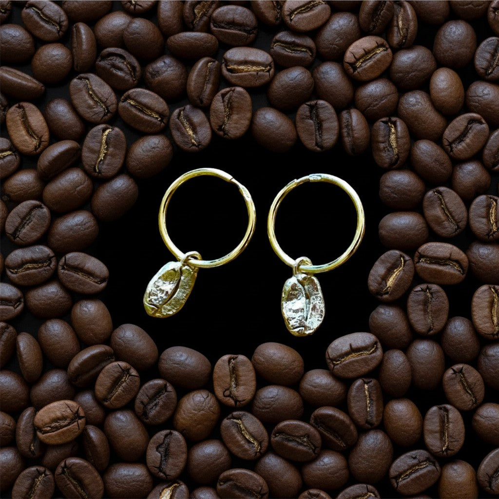 Orecchini a cerchietto MandalaT in oro con pendente a forma di chicco di caffè su sfondo di chicchi tostati