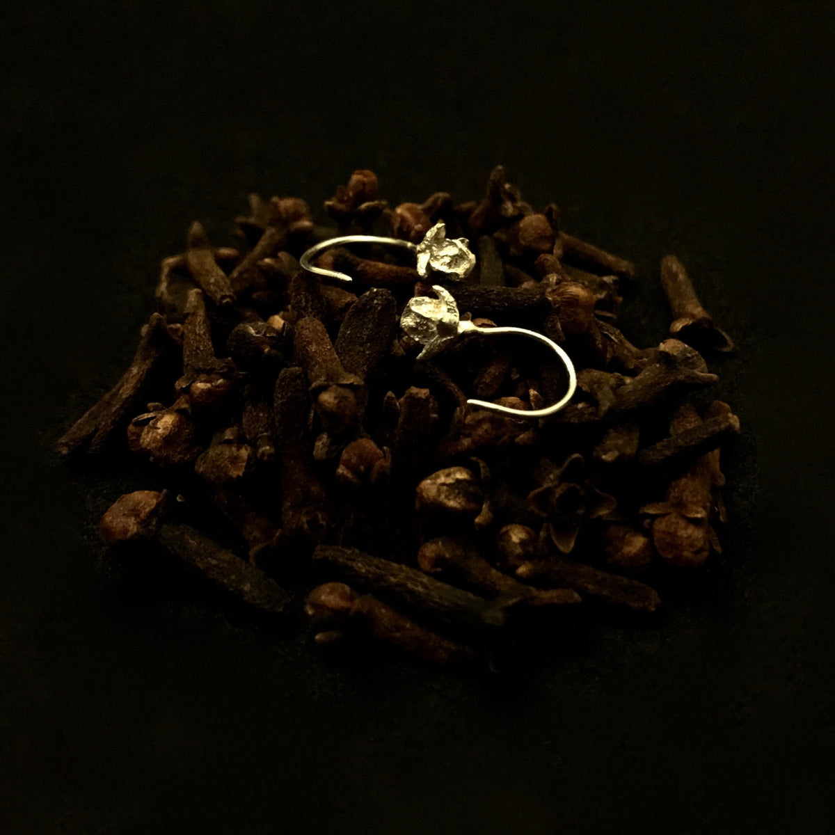 Orecchini MandalaT a forma di chiodo di garofano in argento, delicati gioielli artigianali su sfondo scuro.