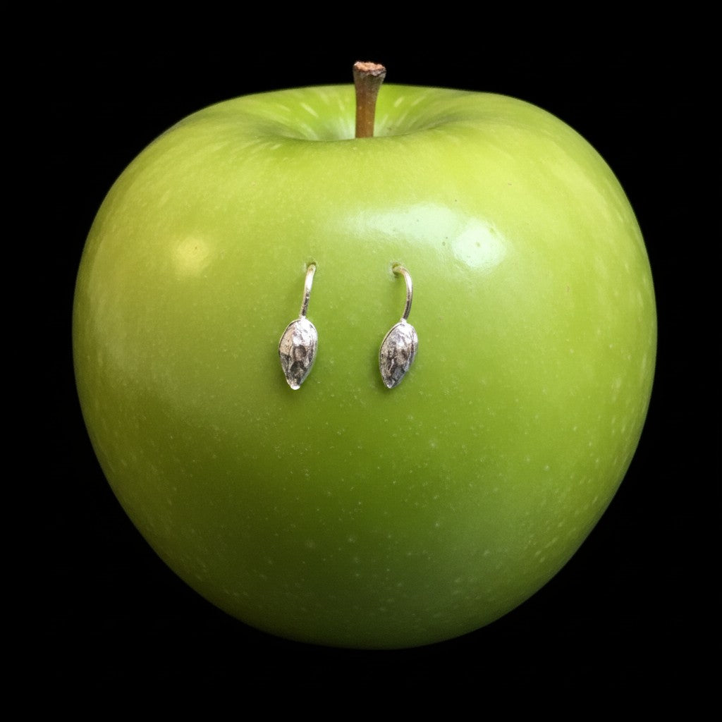 Orecchini MandalaT Seme di Mela in argento a forma di goccia poggiati su una mela verde brillante