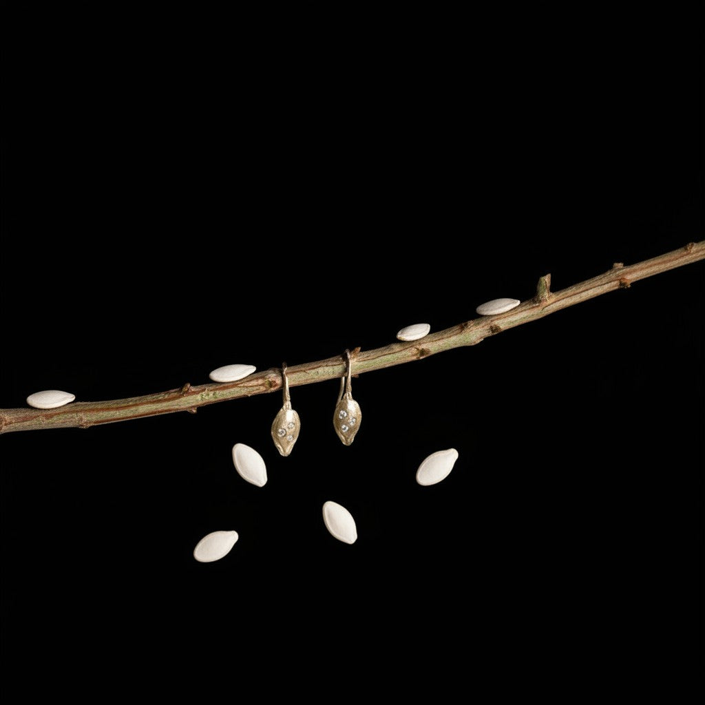 Orecchini MandalaT a forma di seme di zucca in metallo dorato con piccoli cristalli, appesi a un ramo naturale.