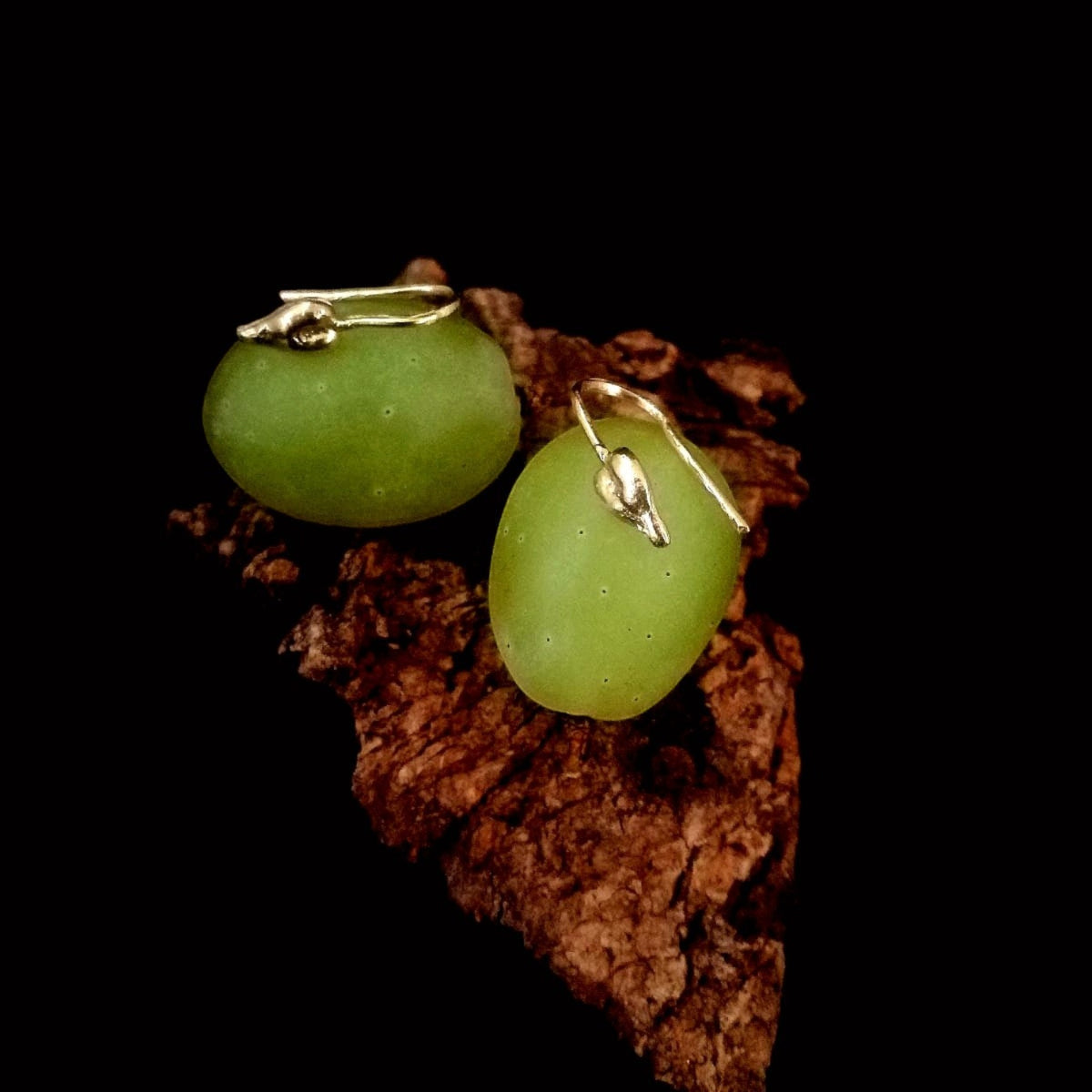 Orecchini MandalaT a forma di vinacciolo in metallo prezioso poggiati su un acino d'uva verde e corteccia