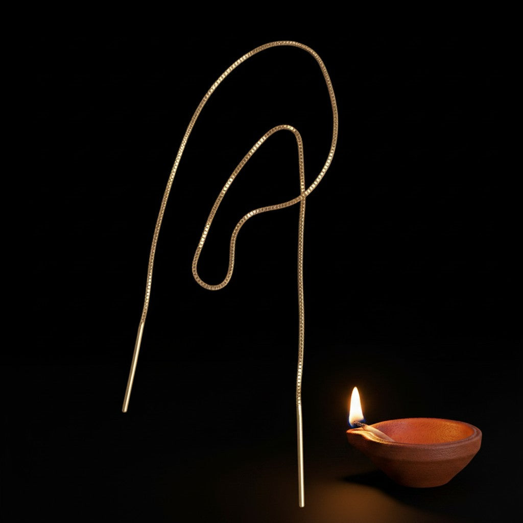Monorecchino MandalaT Luce in oro bianco 18 carati, design a filo lungo 29,5 cm accanto a una piccola lampada a olio.